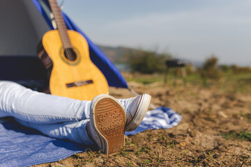 Close up of woman feet lying in front of tent next to acoustic guitar. Freedom and lifestyle concept.