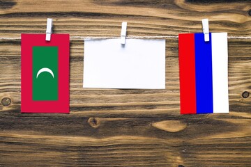 Hanging flags of Maldives and Russia attached to rope with clothes pins with copy space on white note paper on wooden background.Diplomatic relations between countries.