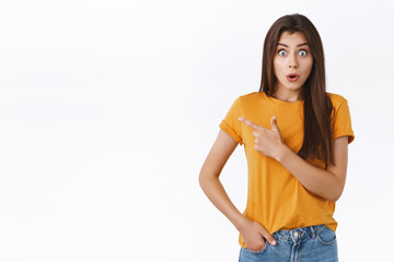 Obraz premium Impressed, fascinated good-looking girl in yellow t-shirt, gasping checking out breathtaking event promo, pointing upper left corner, gasping and staring camera speechless from shock and excitement