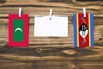 Hanging flags of Maldives and Swaziland attached to rope with clothes pins with copy space on white note paper on wooden background.Diplomatic relations between countries.