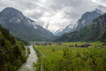 Fototapeta na wymiar Charming panorama view of aare river, meadow and houses in small village in rural area of Switzerland on cloudy sky and mountain background with copy space