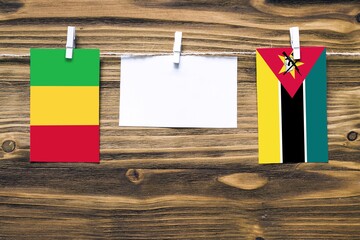 Hanging flags of Mali and Mozambique attached to rope with clothes pins with copy space on white note paper on wooden background.Diplomatic relations between countries.