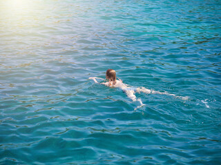 Young slender European girl in swimsuit swimming in clear blue transparent sea water. She enjoying her summer holidays.
