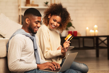 Happy african-american couple looking at laptop and buying online - Powered by Adobe