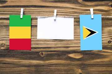 Hanging flags of Mali and Saint Lucia attached to rope with clothes pins with copy space on white note paper on wooden background.Diplomatic relations between countries.