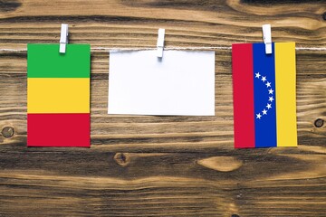 Hanging flags of Mali and Venezuela attached to rope with clothes pins with copy space on white note paper on wooden background.Diplomatic relations between countries.