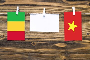 Hanging flags of Mali and Vietnam attached to rope with clothes pins with copy space on white note paper on wooden background.Diplomatic relations between countries.