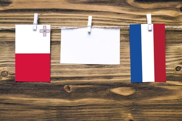 Hanging flags of Malta and Netherlands attached to rope with clothes pins with copy space on white note paper on wooden background.Diplomatic relations between countries.