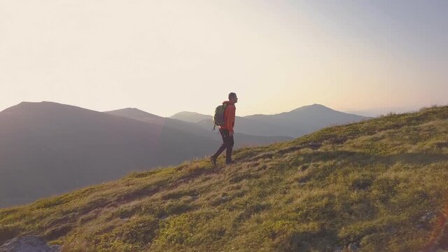 Tourist hiker with a backpack in orange jacket walking on mountain path in Carpathian mountains.
