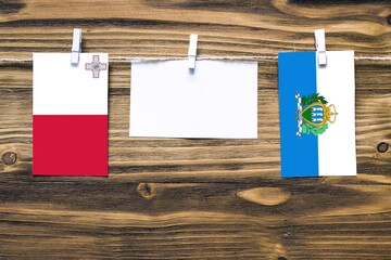 Hanging flags of Malta and San Marino attached to rope with clothes pins with copy space on white...