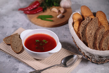 Beetroot soup with parsley in a plate, closeup. Tasty and hearty dinner. Borsch with vegetables, bread box with bread on a gray background. Still life