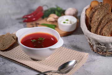 Tasty and hearty dinner. A plate with borsch on the table, next to the board are vegetables, parsley, dill, green onions, garlic, chili peppers, cherry tomatoes, and bread.