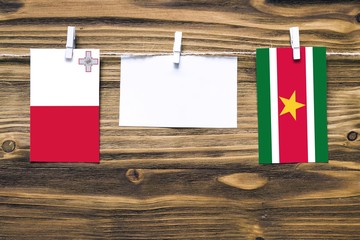 Hanging flags of Malta and Suriname attached to rope with clothes pins with copy space on white note paper on wooden background.Diplomatic relations between countries.