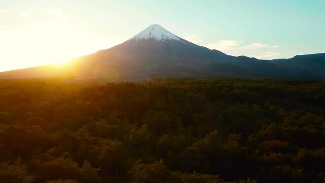 Volcano aerial tracking shot away over forrest with sun setting in Patagonia