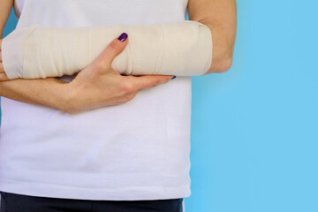 Obraz premium Close up of a woman white long arm plaster, broken hand on blue background.