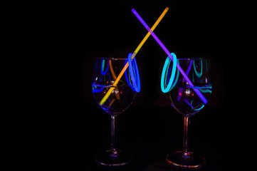 Cocktail wine glass filled with exotic illuminated refreshing juicy liquid and colorful straw with black background for nightlife party