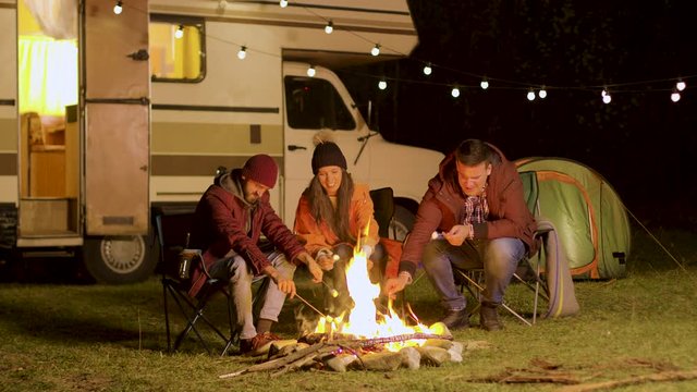 Group of happy friends around burning camping fire