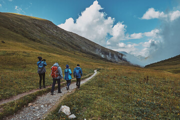 Fototapeta na wymiar A group of hikers walking down a mountain trail, clouds in a gorge in the background. Bzerpinskiy Karniz