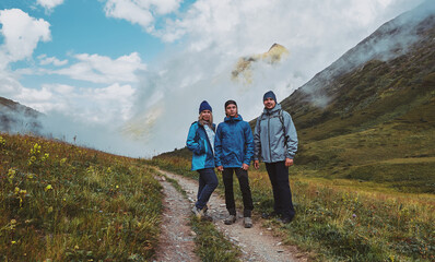 3 hikers standing on a mountain trail, clouds in a gorge in the background. Bzerpinskiy Karniz