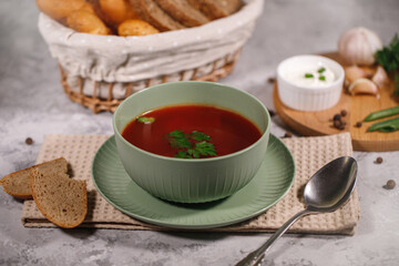 Beetroot soup with parsley in a plate, closeup. Tasty and hearty dinner. Borsch with vegetables on a gray background.