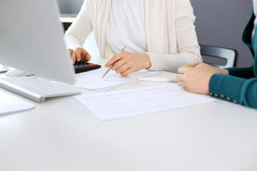 Accountant checking financial statement or counting by calculator income for tax form, hands close-up. Business woman sitting and working with colleague at the desk in office. Audit concept