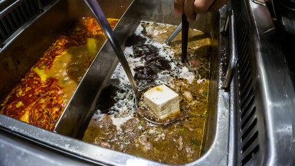 The close up view of a metal ladle dipping a cold tofu into a boiling soup