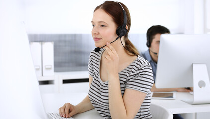 Group of operators at work. Call center. Focus on beautiful woman receptionist in headset at customer service. Business concept and casual striped clothing style