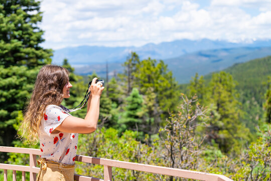 Woman taking picture of Carson National Forest green pine trees with Sangre de Cristo mountains on summer peak overlook from route 76 high road to Taos