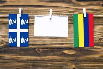 Hanging flags of Martinique and Mauritius attached to rope with clothes pins with copy space on white note paper on wooden background.Diplomatic relations between countries.