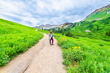 Fototapeta na wymiar Albion Basin, Utah summer with wide angle of woman standing on steep road landscape view on meadows trail in Wasatch mountains wildflowers