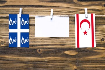 Hanging flags of Martinique and Northern Cyprus attached to rope with clothes pins with copy space on white note paper on wooden background.Diplomatic relations between countries.