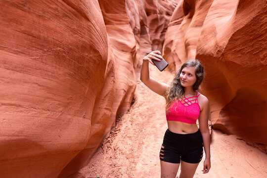Young woman girl taking selfie photo with phone on hike by wave shapes at Antelope slot canyon in Arizona during summer with sports shorts and bra