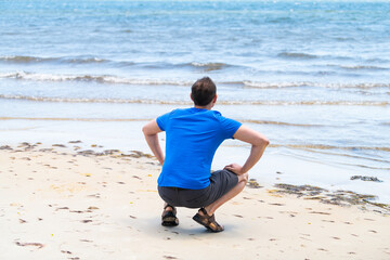 Young man back squatting crouching sitting on beach bay shore sand in Florida near Pensacola
