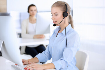 Call center office. Beautiful blonde woman using computer and headset for consulting clients...
