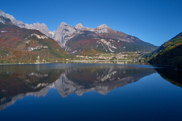 Fototapeta na wymiar Aerial view of Lake Molveno, north of Italy in the background the city of Molveno, Alps, blue sky. Reflection of mountains in water. Autumn season. Multi-colored palette of colors