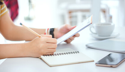 Closeup of hand. young female writing on notebook while she reading information from paperwork
