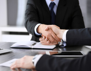 Businessman shaking hands with his colleague or partner above the glass desk in modern office, close-up. Unknown business people at meeting. Teamwork, partnership and handshake concept