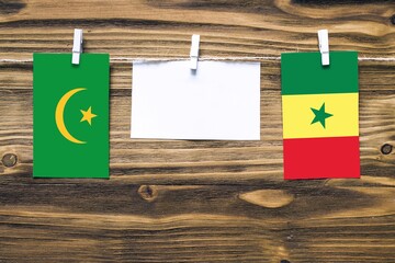 Hanging flags of Mauritania and Senegal attached to rope with clothes pins with copy space on white note paper on wooden background.Diplomatic relations between countries.