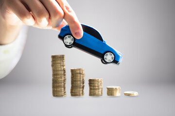 Person's Hand Holding Model Toy Car Over Stacked Of Coins