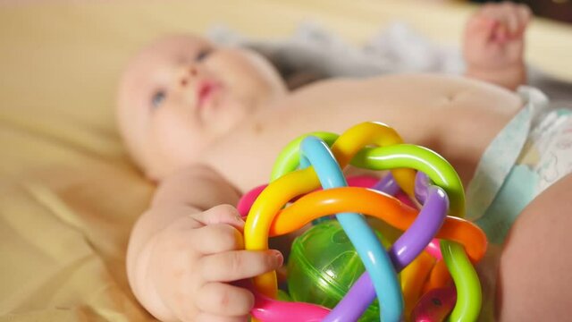 Four months baby playing with rattle on bed in defocus. Close up of baby rattles. Sensory development of a child. Close up shot.