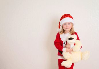 Little girl wearing a santa hat holding a toy bear isolated on white background. Merry Christmas and Happy New Year!