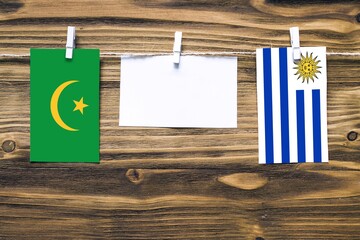 Hanging flags of Mauritania and Uruguay attached to rope with clothes pins with copy space on white note paper on wooden background.Diplomatic relations between countries.