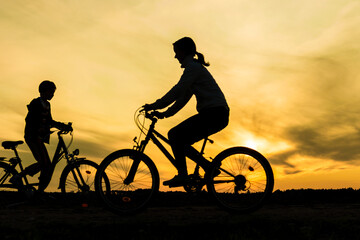 Obraz premium Boy and young girl riding bikes in different directions, silhouettes of riding persons at sunset in nature