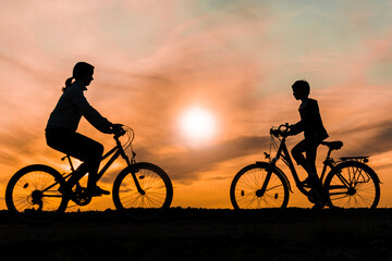 Boy and young girl riding bikes in different directions,  silhouettes of riding persons at sunset in nature