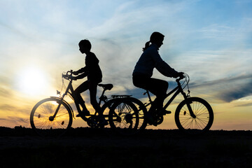 Boy and young girl riding bikes in different directions,  silhouettes of riding persons at sunset in nature