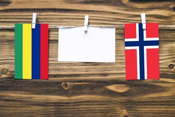 Hanging flags of Mauritius and Norway attached to rope with clothes pins with copy space on white note paper on wooden background.Diplomatic relations between countries.