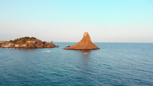 Golden hour Aerial push in: sea rock formation and boats passing by