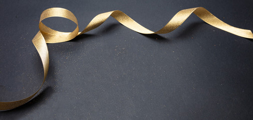 Golden satin ribbon on black background, copy space