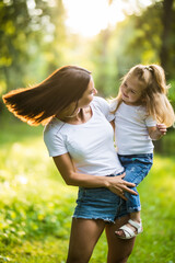 Happy young mother and daughter laughing together outdoors in green park