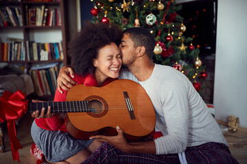 family in front of decoration Christmas tree. man surprise woman a with a guitar gift for Christmas.
